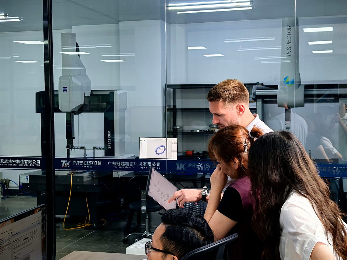 Overseas customer and engineering team review technical documents on laptop, ZEISS CMM metrology lab background