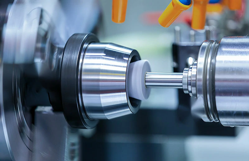 Precision CNC cylindrical grinding machine in operation, finishing a metal shaft with coolant nozzles — tight tolerance grinding services